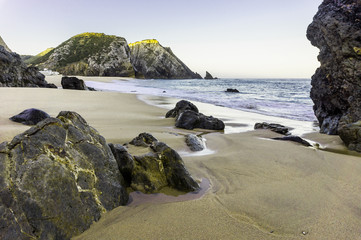 Ocean wave and rock cliffs on sandy beach, Portugal