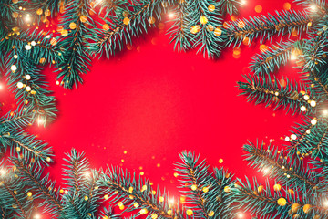 Fir branches with blurred lights garland on a red background. Christmas wallpaper. Flat lay, copy space.