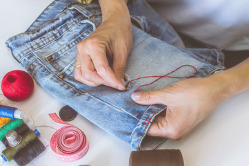 women's hands, a tailor sews clothes at a table on which spools of thread lie