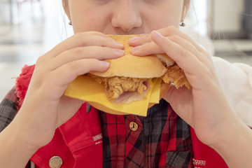 hungry teenage girl eating a cheeseburger on the food court of the mall. Unhealthy food.