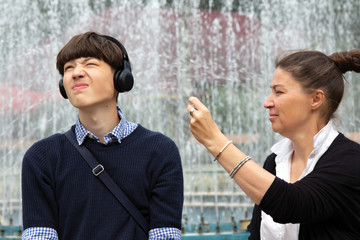 A middle-aged woman, a mother, is trying to get attention from the son of a teenager who listens to music with large headphones. Family resting together on the weekend.