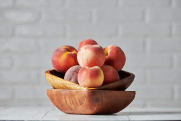 Peaches in wooden bowl with white brick wall background