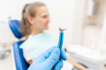 Close-up hand of dentist in the glove holds dental high speed turbine. The patient in blue chair at the background. Office where dentist conducts inspection and concludes.