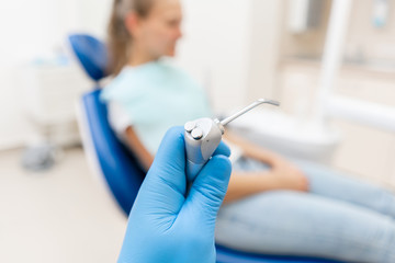 Close-up hand of dentist in the glove holds Gun dental water and air. The patient in blue chair at the background. Office where dentist conducts inspection and concludes.