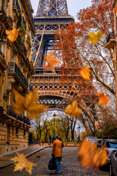 A guy under the Eiffel tower in autumn with falling leafs