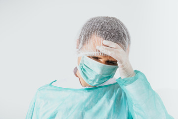 Headache of a surgeon, a doctor. A man wearing a green surgical apron and a face mask on a bright background is holding his head. Medical and pharmaceutical concept. Health problems before surgery.