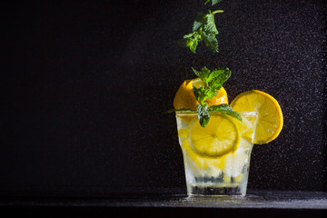 Lemonade with flying mint and lemon. Summer refreshing drink with lemon on dark background. Infused water with citrus and mint. Levitation. Horizontal