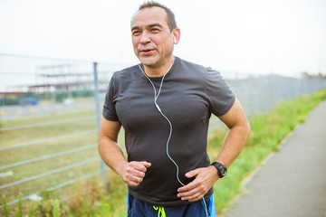 Mature man doing jogging on a city street. Senior man leads a healthy and active lifestyle playing sports.