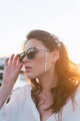 A beautiful girl in dark sunglasses and with beautiful styling is standing on the pier by the river. Girl in pearl jewelry and glasses.
