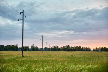 Fototapeta na wymiar sunset over green field with electricity pylons