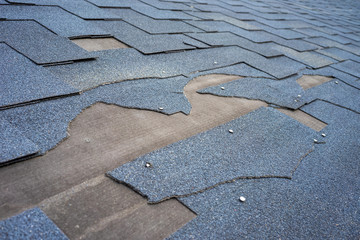 Сlose up view of bitumen shingles roof damage that needs repair.