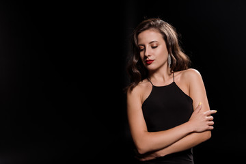 attractive young woman in dress standing with crossed arms isolated on black