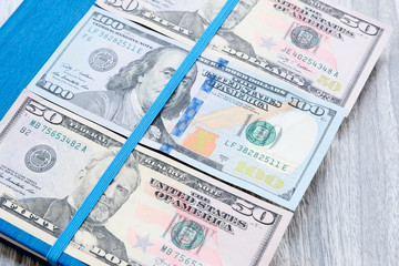 Fototapeta na wymiar Dollars on a blue notebook. American banknotes of different denominations . Wooden marble Board background. The problem of budgeting, calculation of estimates. The concept of profitable investment.