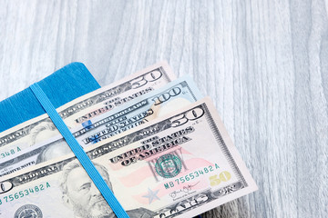 Dollars on a blue notebook. American banknotes of different denominations . Wooden marble Board background. The problem of budgeting, calculation of estimates. The concept of profitable investment.