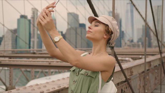 French tourist takes selfies while walking by Brooklyn Bridge, first time in New York, moment from tourist's life, New York's destination.