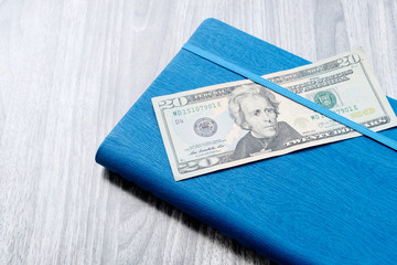 A twenty-dollar bill with a blue notebook. Wooden marble Board background. The problem of budgeting, calculation of estimates. The concept of profitable investment.