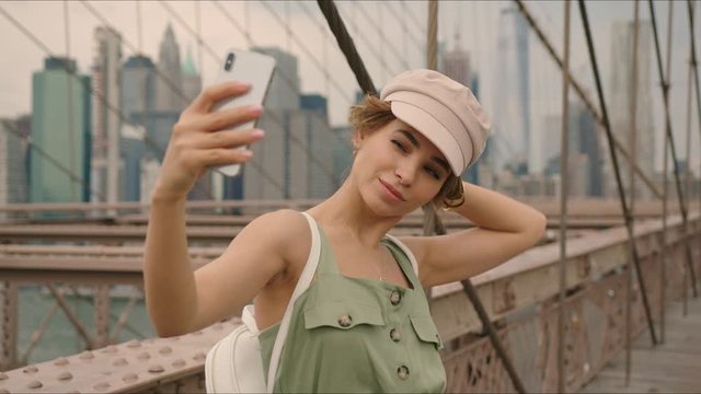 French tourist takes selfies while walking by Brooklyn Bridge, first time in New York, moment from tourist's life, New York's destination.