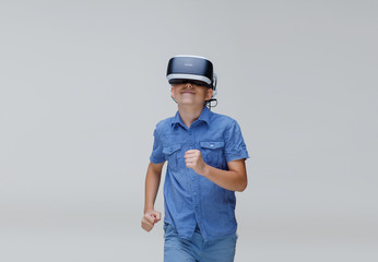 Young happy boy in glasses of virtual reality on gray background. Augmented reality, game, future technology concept. VR.