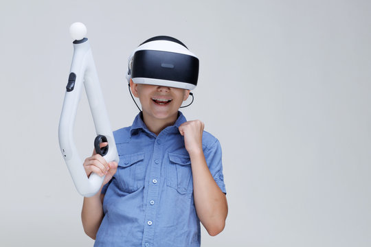 Young happy boy in glasses of virtual reality with controller in hands on gray background. Augmented reality, game, future technology concept. VR.