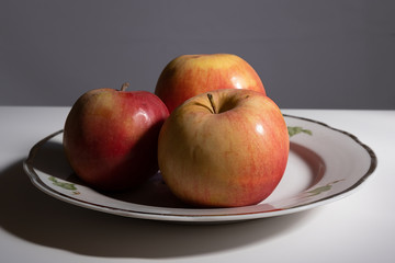 Three apples on a plate on a table in the kitchen. Low key