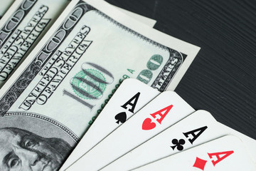 Four aces with american dollars lie on a black wooden background.