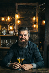 Man drinks a cocktail. Barman hipster. Alcoholic with bottle and glass drinking martini at night.