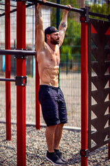 Obraz premium Strong Muscular bearded man doing abdominal exercise on horizontal bar at street gym yard. Strength and motivation. Outdoor workout. fitness, sport, exercising, training and lifestyle concept .