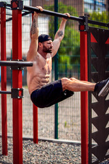 Fototapeta premium Strong Muscular bearded man doing abdominal exercise on horizontal bar at street gym yard. Strength and motivation. Outdoor workout. fitness, sport, exercising, training and lifestyle concept .