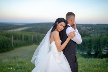 Beautiful bride hugging her groom from behind  on top of mountain in the evening