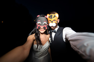 Funny wedding couple in mask taking selfie on black background at night
