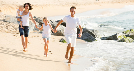 parents with two kids jogging on beach .