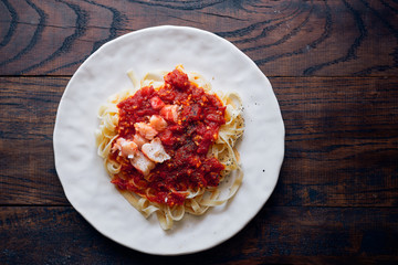 Hot homemade pasta with tomato sauce and shrimps with spices and herbs in plate on a wooden table top view 