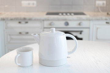Fototapeta na wymiar white ceramic teapot and cup on a white table against the background of a light kitchen of a classic interior with gentle lighting