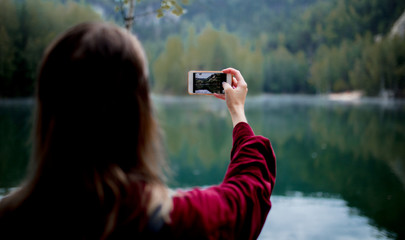 woman in hat and red shirt with mobile phone near lake