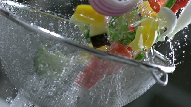 Cook&rsquo;s hand washes pieces of fresh vegetables under running water with a colander tossing them. Garnish concept and and vegetarian food. Slow motion