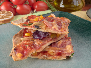 Pizza on thin dough.With slices of salami and ham ,olives and tomatoes.On a background of vegetables.