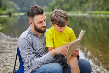 Family are reading book near river. - obrazy, fototapety, plakaty