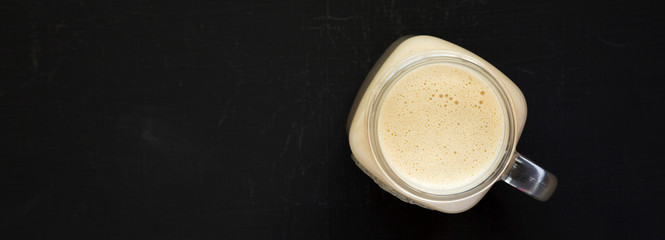 Peanut butter banana smoothie in a glass jar mug on a black surface, top view. Flat lay, from above, overhead. Copy space.