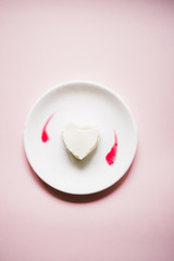 Hard shaped panna cotta with raaspberry couls on a white dish over a gray background