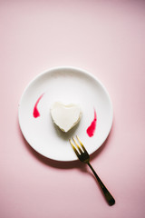 Hard shaped panna cotta with raaspberry couls on a white dish over a pink background