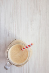 Peanut butter banana smoothie in a glass jar on a white wooden background, overhead view. Top view, flat lay, from above. Copy space.