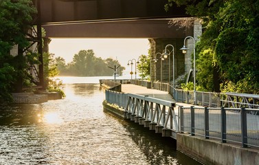 A walkway going along water canal and under the highway overpass - obrazy, fototapety, plakaty
