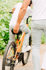cropped view of father holding sit of bicycle while son riding