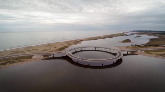 A drone shot over Puente Laguna Garzon, Uruguay on a cloudy day. A single car drives over the ring-road bridge across to the other side.