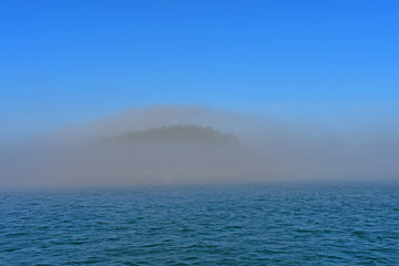 Obraz premium Morning fog hugs the coast of Deception Pass as it enters the Salish Sea in Washington State