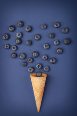 Ice cream cone filled with .blueberries on a blue textile background. Berries .fall out from a waffle cone. Summer concept.
