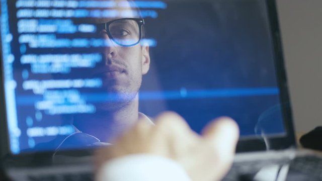 Double Exposure Shot of Man Hacker Programmer in Eyeglasses working at a laptop. Reflection in monitor: Developer writes blue code and and Drinking Tasty Coffee.
