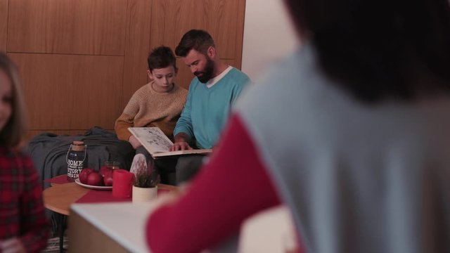 Family time ather mother son and daughter reading children book drink tea on a sofa in evening home smile woman lamp girl living love male night parenting room sitting young apartment cozy slow motion