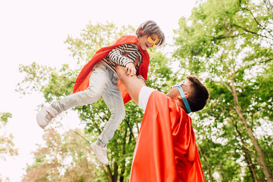 father in superhero costume holding son in hands while kid laughing and looking at dad