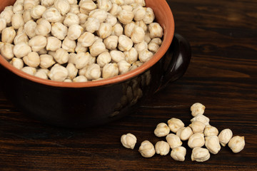 Raw chickpeas in a ceramic bowl on a dark wooden background. top view, out of range.